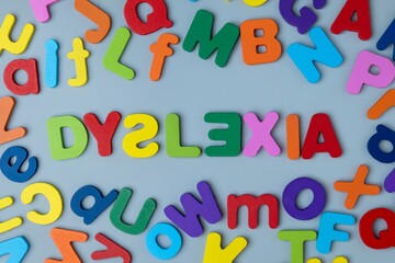Fototapeta premium The word DYSLEXIA is spelled out in colorful wooden letters scattered on a gray background. Learning difficulties, neurodiversity, educational challenges, reading struggles, and cognitive support.