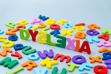 Naklejka premium The word DYSLEXIA is spelled out in colorful wooden letters scattered on a gray background. Learning difficulties, neurodiversity, educational challenges, reading struggles, and cognitive support.