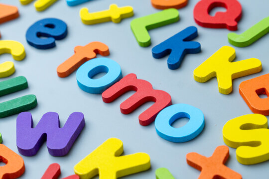 Colorful wooden alphabet letters arranged to form the word FOMO. Fear of missing out, digital anxiety, social pressure concept.