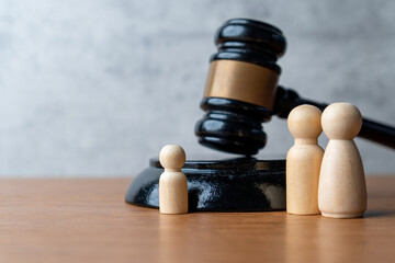 A wooden gavel stands next to three wooden peg dolls. Family law, guardianship, child custody,...