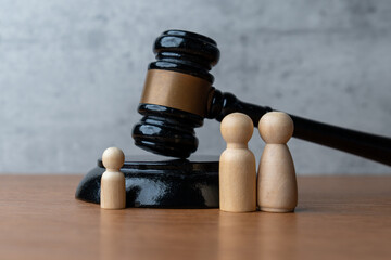 A wooden gavel stands next to three wooden peg dolls. Family law, guardianship, child custody,...