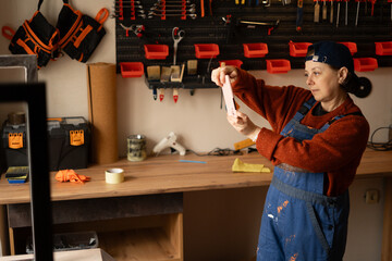 Young professional mechanic or craftsman woman in blue overalls take photo on mobile phone fix work result in repair renovation workshop.