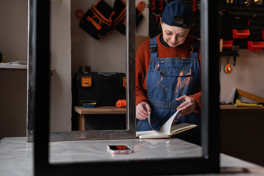 Woman in blue coveralls working with technical drawings with tools, furniture making or restoration renovation process in workshop. small business and start-up
