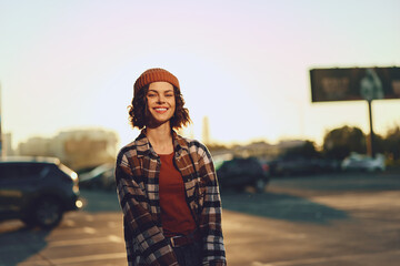Woman smile candid urban beanie lifestyle portrait in a sunlit parking lot at golden hour glow,...