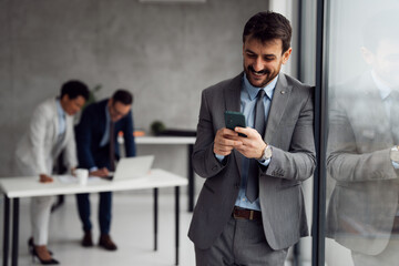 Businessman using his mobile phone in an office, with colleagues working in the background.