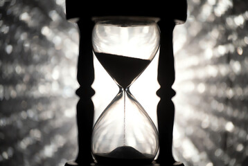 Falling sand in a clear glass hourglass, casting a prominent blurred shadow on a light wall, symbolizing the steady passage of time, deadlines, and patience.