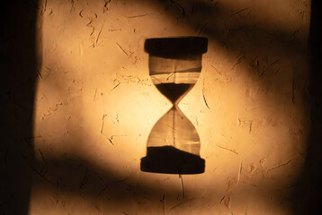 Dramatic shadow of an hourglass on a warm, textured wall, symbolizing the relentless passage of time, urgency, deadlines, and limited opportunity.