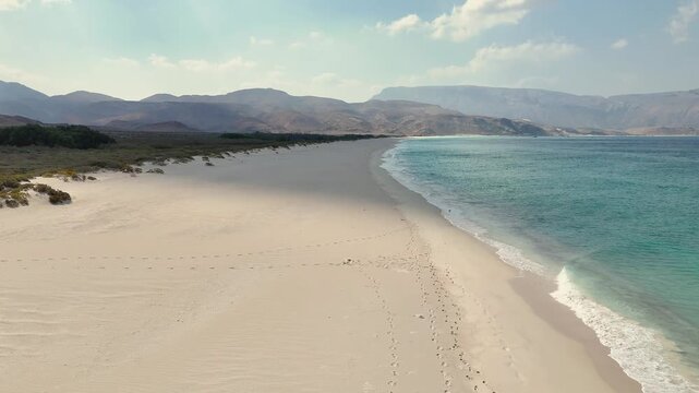 Drone view of stunning coastal landscape with clear turquoise water, soft white sand, and towering rocky cliffs, where small boats create a serene and picturesque seaside atmosphere. Socotra island