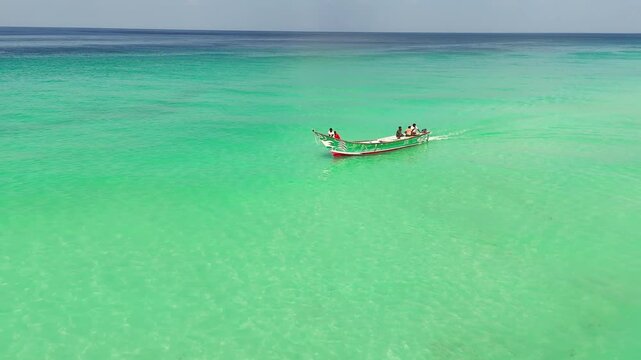 Boat glides over clear turquoise water from above. A lone boat moves across crystal-clear turquoise water, drone view, creating a serene and minimalistic seascape with vibrant, tropical tones.