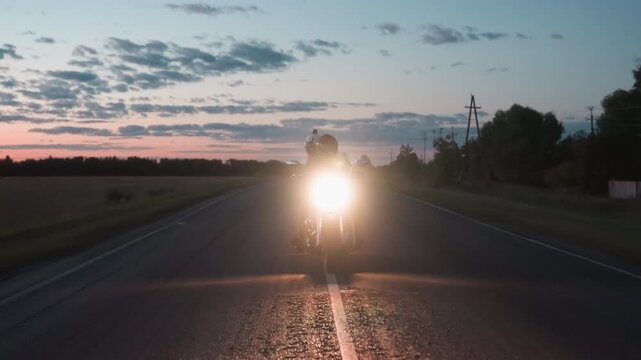 Night racer speeding on open rural road under fading sunset sky, motorcycle headlight shining brightly as powerlines, trees, and kilometer signpost frame countryside backdrop