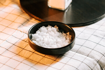 Bowl of salt placed on a checkered tablecloth near a container in a cozy dining setting