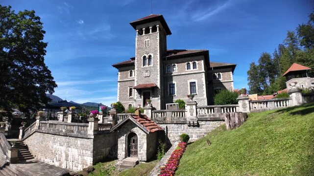 Cantacuzino Castle, a prominent architectural landmark in Busteni, Romania, showcasing its historic stone facade, traditional windows, and an elaborate stone balustrade under a clear blue sky in