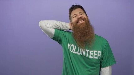 Man with long beard wearing green volunteer shirt scratches neck and smiles in bright studio; relaxed.