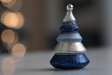 Sapin décoratif bleu et argent posé en intérieur avec bokeh lumineux en arrière-plan et espace négatif copyspace pour fêtes de Noël, fin d’année et réveillons
