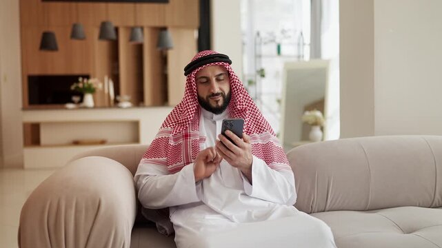 Arab man in traditional clothing scrolling social media app on phone, e-banking