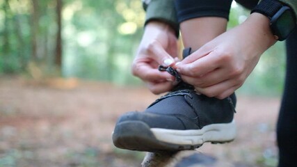 Unrecognizable woman athlete tying up laces on her sneakers, fixing shoes during workout in forest, tracking shot