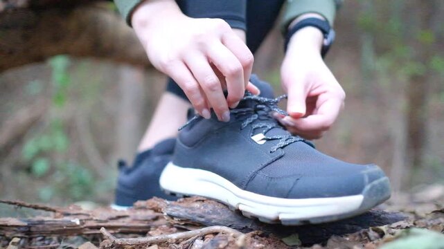 Unrecognizable woman athlete tying up laces on her sneakers, fixing shoes during workout in forest, tracking shot