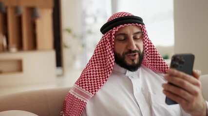 Smiling Muslim man in headscarf having video call on phone, chatting with friend - Powered by Adobe