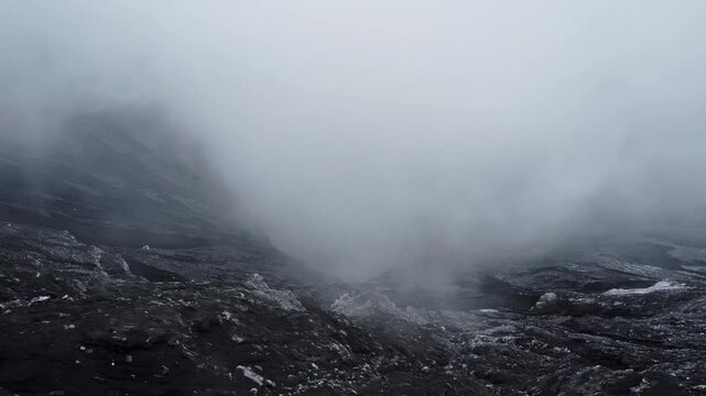 Calm drone orbit shot capturing the active crater of Mount Bromo, Java. White steam and smoke drift over the dark, rugged rock, creating a moody, dramatic volcanic scene.