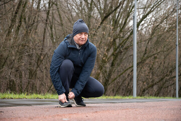 Adult sporty man tying shoelaces before training and outdoor workout at public park. Preparation for workout. Outdoors.