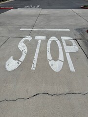 Pavement STOP Marking: The word STOP painted in white on asphalt road surface in a residential community as a warning to drivers ahead of an intersection.