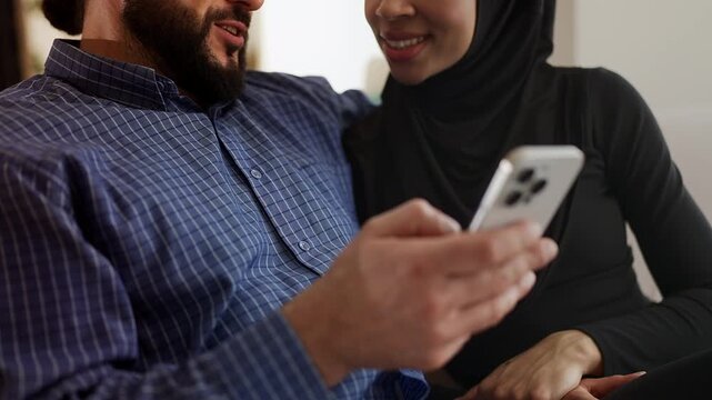 Cheerful Muslim couple choosing luxurious items on phone, mobile shopping app