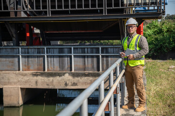 Engineer standing confidently at a hydraulic water control structure during a sunny field inspection