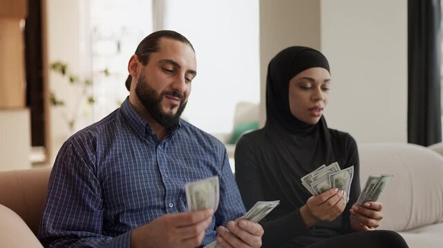 Happy Muslim couple counting dollars and hugging, celebrating finances