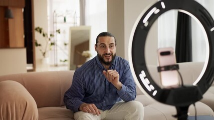 Cheerful Arab man recording lifestyle vlog on phone at home, giving advice