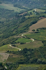 Aerial view of a dramatic, winding road curving through the lush green hills and valleys of Emilia-Romagna