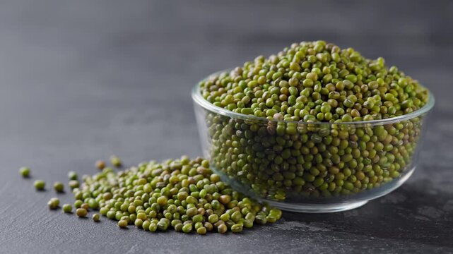 mung beans in a glass plate and scattered on a black marble background.  green mung beans in a clear glass bowl on a dark kitchen table.
