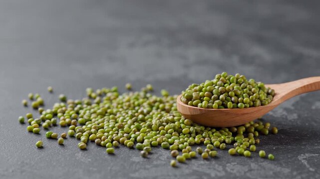mung beans in a wooden spoon on a black marble background.  green mung beans in a wooden spoon on a dark kitchen table.