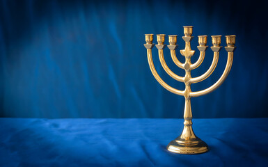 Fototapeta premium A golden menorah with seven branches sits on a blue fabric surface, symbolizing the jewish holiday of hanukkah and its traditions of light and faith