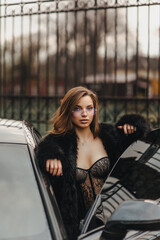 Photo, portrait of a beautiful young sexy woman, a model girl with a chic expensive black car on a city street.