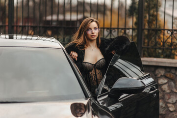 Photo, portrait of a beautiful young sexy woman with glasses, a model girl in lingerie, in a fur coat with a chic expensive black car on a city street outdoors.