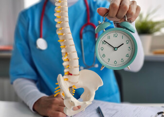 Doctor shows human spine model with clock in hand to discuss time