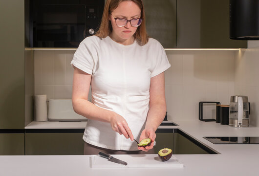 woman standing in a modern kitchen, slicing a ripe avocado on a cutting board. She prepares fresh - Powered by Adobe
