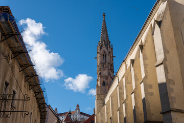 Gothic tower of the Clarissine Church in Bratislava old town, with historic buildings and clear blue sky in the background.

