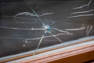 Close-up of a cracked window glass with a central impact point that resembles damage from a possible projectile.