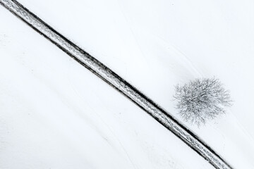 Winter aerial composition with a lone tree and diagonal snowy road in the Liptov countryside