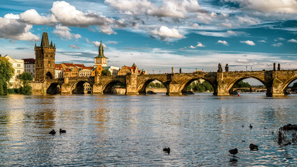 Charles Bridge in Prague with historic towers and the Vltava River under a bright sky with clouds in a scenic daylight city landscape