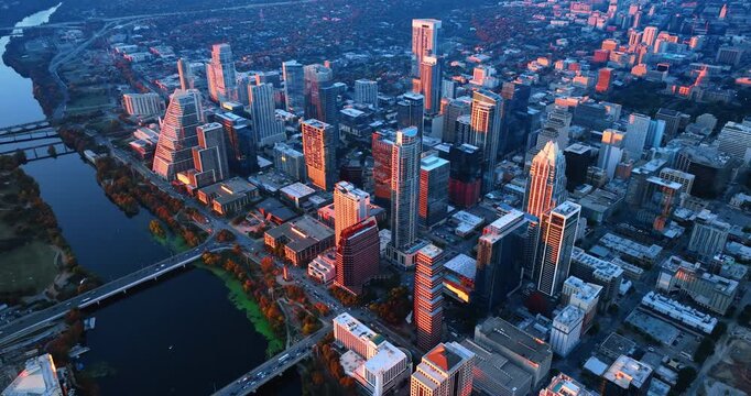 Approaching the densely built downtown of Austin, Texas, USA. Sunset colors the tops of high-rises at the waterfront of the Colorado River. Aerial view.