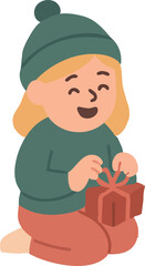 A cheerful little girl in a green winter hat and sweater happily opens a wrapped gift while kneeling on the floor.