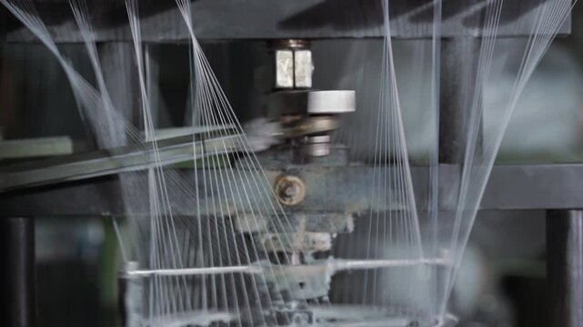 industrial knitting machine producing fine mesh, close-up view of circular needles forming delicate netting from yarn metallic components and spools visible,