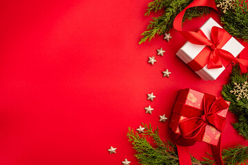 Christmas background with gift boxes with red ribbons, green pine branches, and golden stars on red...