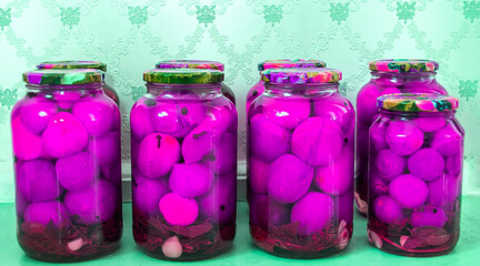 Bright pink pickled vegetables displayed in jars on a colorful background in a kitchen setting