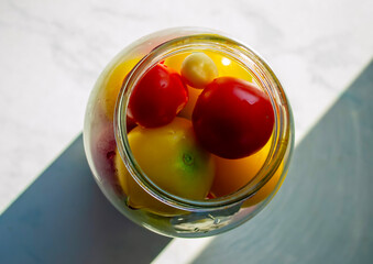 Brightly colored tomatoes in a glass jar sitting on a sunny countertop in a kitchen