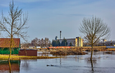 Quiet scene of a flooded area with trees and an industrial building in the background during early spring