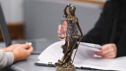 Bronze statue of Lady Justice holding scales, symbolizing law and fairness, placed on a desk with...