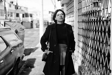 Woman walking city street wearing trench coat and glasses